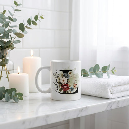 Personalisierte Keramiktasse mit Blumen-Initiale L auf weißem Marmor neben brennenden Kerzen und Eukalyptuszweigen, cozy Wohndeko Geschenkidee