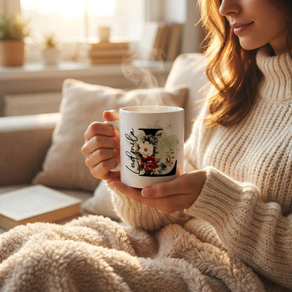 Frau in Wollpullover hält dampfende personalisierte Keramiktasse mit floralem Anfangsbuchstaben und Name, gemütliche Cozy-Atmosphäre im Wohnzimme